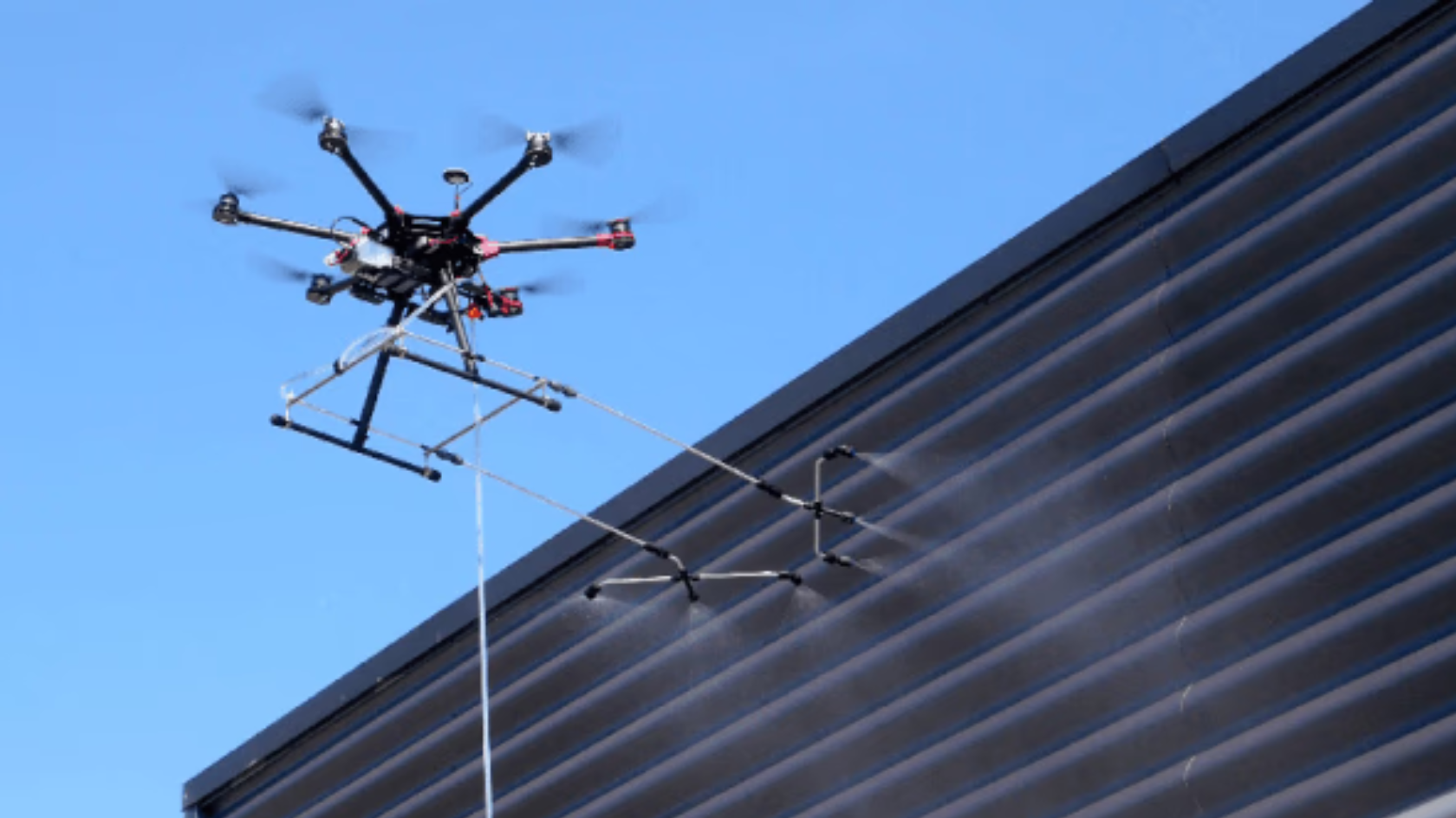 Drone de nettoyage pulvérisant un bardage métallique de bâtiment industriel